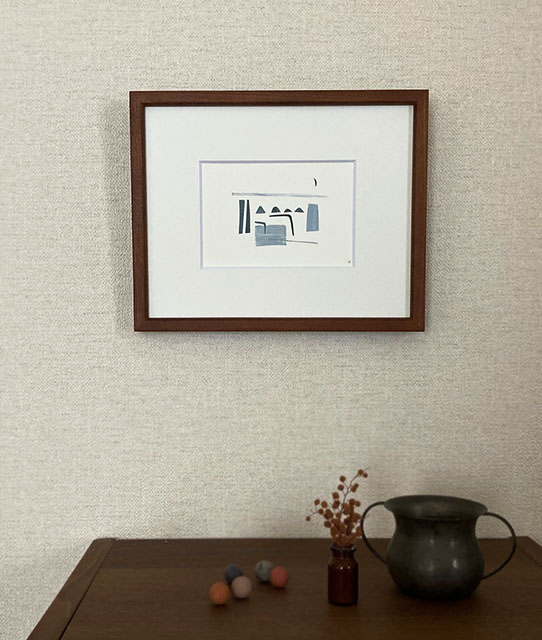 青い幾何学模様と三日月が描かれた幾何学的な旅の風景 / ka_waの額入りプリントが、小さな花瓶と金属製のボウルが置かれた木製のコンソールテーブルの上に飾られ、モダンアートの魅力を際立たせている。.